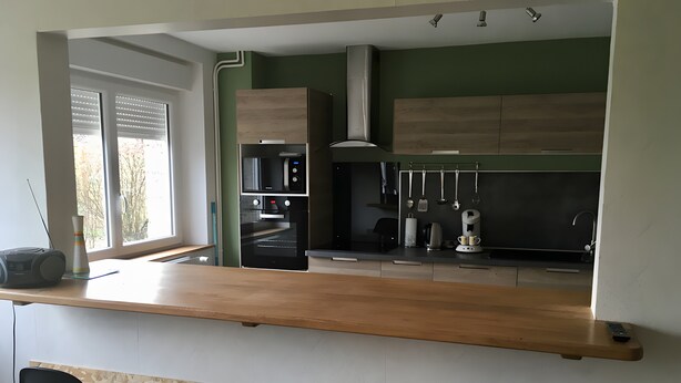 A modern kitchen with a wooden countertop, built-in appliances, and a bar area with stools.