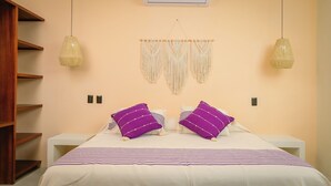 A bedroom with a bed, two purple pillows, a macrame wall hanging, and two pendant lights. - Luxury villa, private pool and brathtaking ocean view — steps from Playa La Ropa (Zihuatanejo)