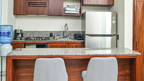 A kitchen with wooden cabinets, a stainless steel refrigerator, a granite countertop, and two bar stools. - Luxury villa, private pool and brathtaking ocean view — steps from Playa La Ropa (Zihuatanejo)
