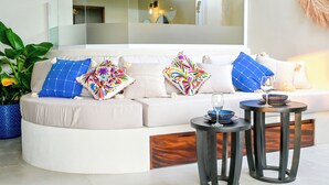 A modern living room with a white sofa, colorful pillows, a small round table with a glass, and a potted plant. - Luxury villa, private pool and brathtaking ocean view — steps from Playa La Ropa (Zihuatanejo)