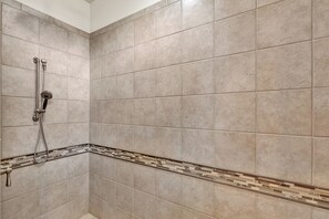 Une salle de bain avec des carreaux de couleur beige, une douche Ă©quipĂ©e dâun pommeau de douche Ă main et une bordure dĂ©corative en carreaux le long du bas du mur.