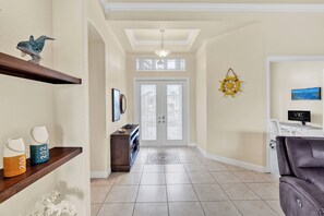 A hallway with a wooden bench, a door with frosted glass panels, a wall-mounted TV, and a sail wheel decoration.