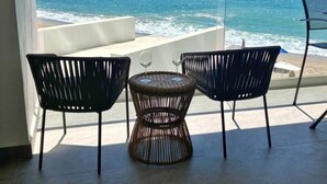 Een balkon met twee stoelen en een tafel, met uitzicht op een strand en de oceaan.