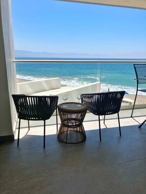 A balcony with two chairs and a table, overlooking a beach and ocean. - Beachfront Condo at Harbor 171 Puerto Vallarta | Ocean Views & Resort Amenities (Puerto Vallarta)
