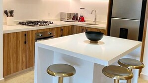 Een moderne keuken met houten kastjes, een centraal eiland met krukken, een inbouwfornuis en een koelkast.