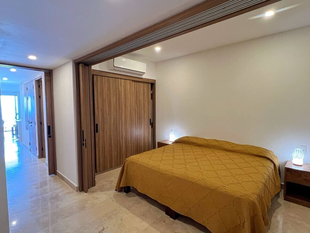 Une chambre à coucher comprenant un lit, une armoire en bois, un appareil de climatisation et une table de chevet avec une lampe.