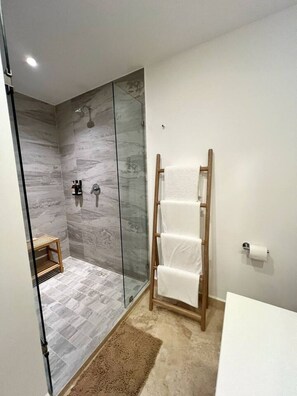 A modern bathroom with a glass shower enclosure, a wooden towel rack, and a white sink. - Beachfront Condo at Harbor 171 Puerto Vallarta | Ocean Views & Resort Amenities (Puerto Vallarta)