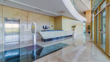 A modern lobby with a reception desk, a glass elevator, and a marble floor.