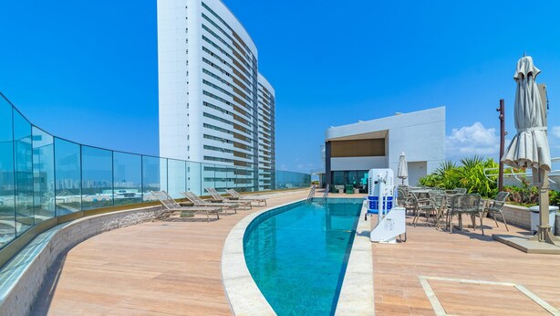 A rooftop pool area with a curved pool, lounge chairs, and a glass balustrade. - Parque do Cais #1109 With Sea View by Carpediem (Recife)