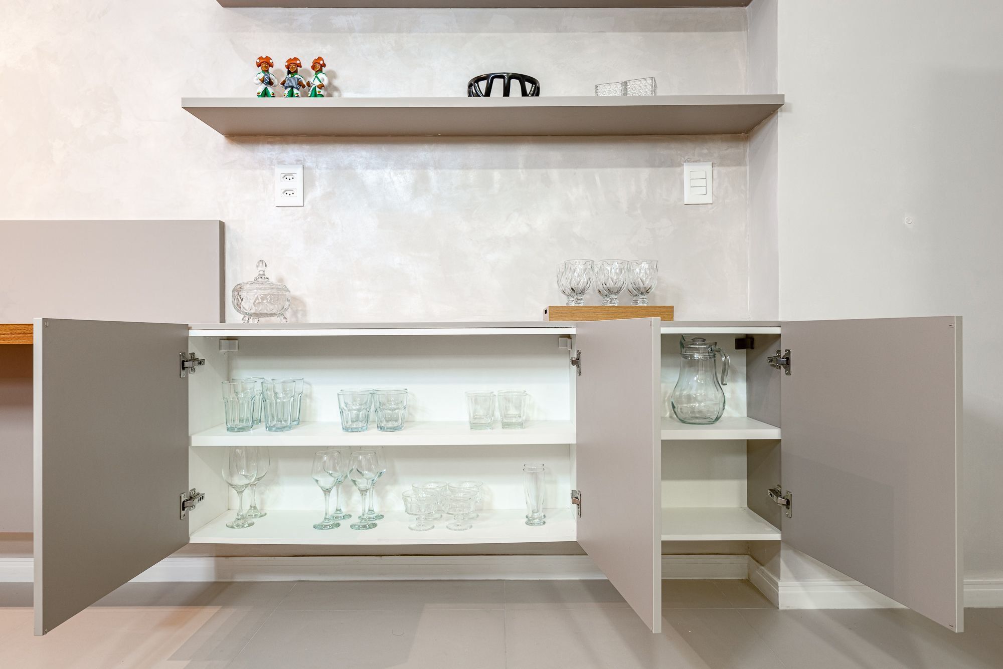 A kitchen with open cabinets displaying glassware and a shelf with decorative items.