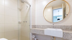 A bathroom with a glass shower enclosure, a white sink with a granite countertop, and a round mirror. - Parque do Cais #1109 With Sea View by Carpediem (Recife)