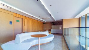 A modern reception area with a curved seating arrangement, a small round table, and a wooden wall. - Parque do Cais #1109 With Sea View by Carpediem (Recife)