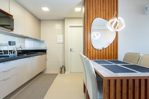A modern kitchen with a built-in microwave, a sink, and a dining area with a wooden table and chairs. - Parque do Cais #1109 With Sea View by Carpediem (Recife)