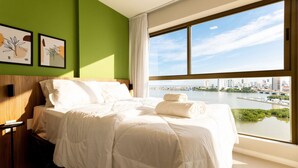 A hotel room with a large bed, green walls, artwork, and a view of a city and water. - Parque do Cais #1109 With Sea View by Carpediem (Recife)
