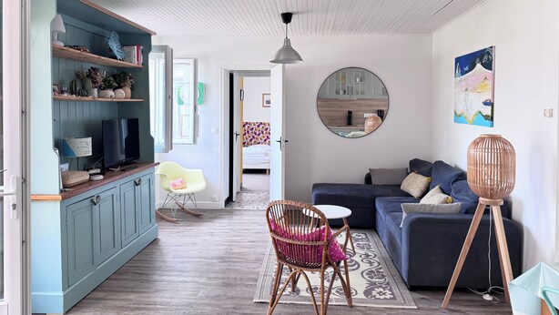 A modern living room with a sofa, a dining area with a table and chairs, a kitchen visible through an open door, and a large round mirror on the wall. - Pointeau House (Saint-Georges-d'Oléron)