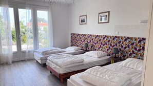 A hotel room with three beds, a large window with sheer curtains, a patterned headboard, and two framed pictures on the wall. - Pointeau House (Saint-Georges-d'Oléron)