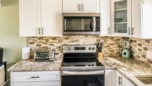 Una cocina moderna con armarios blancos, un microondas, una estufa y una licuadora.
