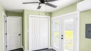 Un dormitorio con cama, ventilador de techo y vista a un paisaje verde por una puerta.
