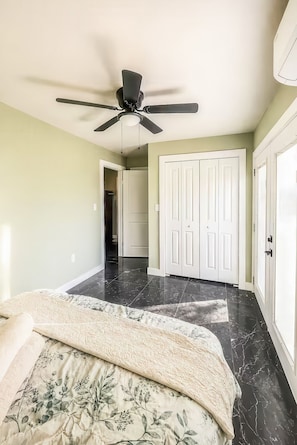 A bedroom with a bed, a ceiling fan, a door, and a hallway.