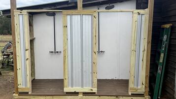 A wooden structure with three vertical panels, possibly a storage or utility unit, with a metal door and a ladder leaning against it.