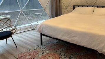 A tent-style room with a bed, a chair, and a large window.