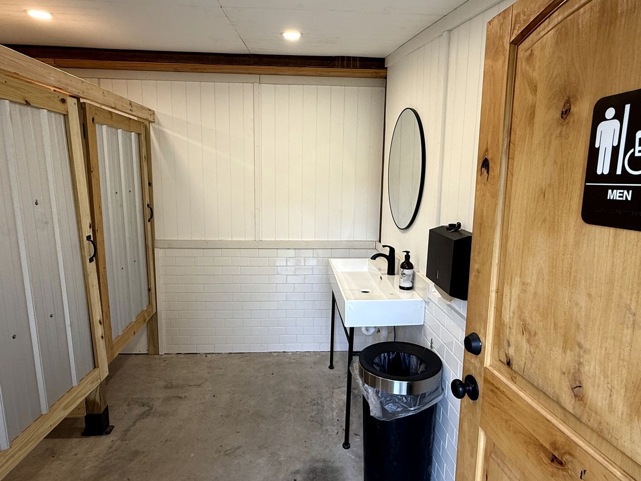 Eine Herrentoilette mit einem weißen Waschbecken, Spiegel und Mülleimer.
