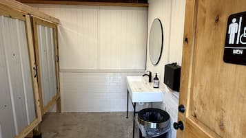 Eine Herrentoilette mit einem weißen Waschbecken, Spiegel und Mülleimer.