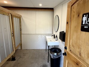 Baño de hombres con lavamanos, espejo y cubo de basura.