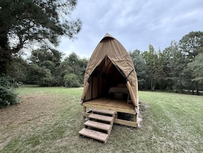 A tent with a wooden platform and steps leading up to it, surrounded by trees.