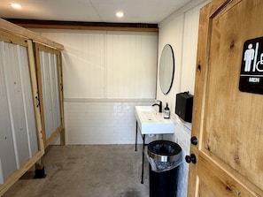 Een herentoilet met een wastafel, spiegel en prullenbak.
