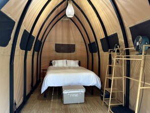 A tent with a bed, a ladder, a chest, and a fan.