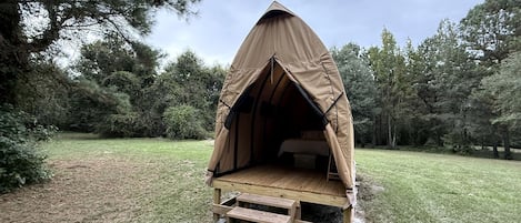 A tent with a wooden platform and steps leading up to it, surrounded by trees.