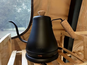 Una tetera negra sobre un soporte de madera con un asa de corcho, ubicada dentro de una estructura parecida a una tienda de campaña.