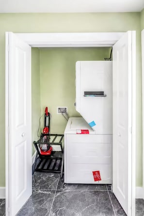 Una habitación compacta con un armario blanco, un aspirador rojo y un estante negro.