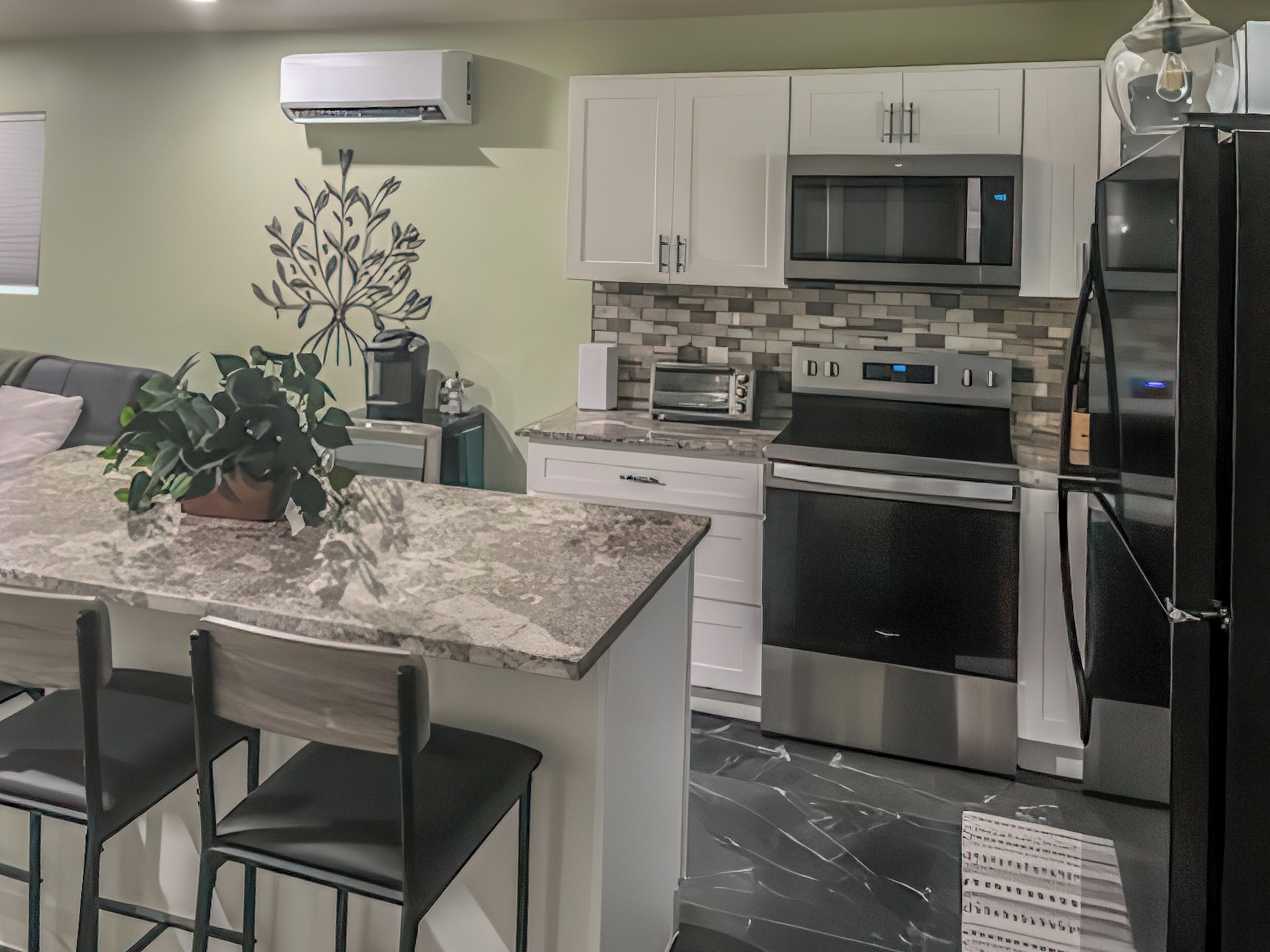A modern kitchen with white cabinets, a black refrigerator, stainless steel appliances, and a marble countertop.