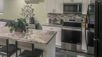 A modern kitchen with white cabinets, a black refrigerator, stainless steel appliances, and a marble countertop.