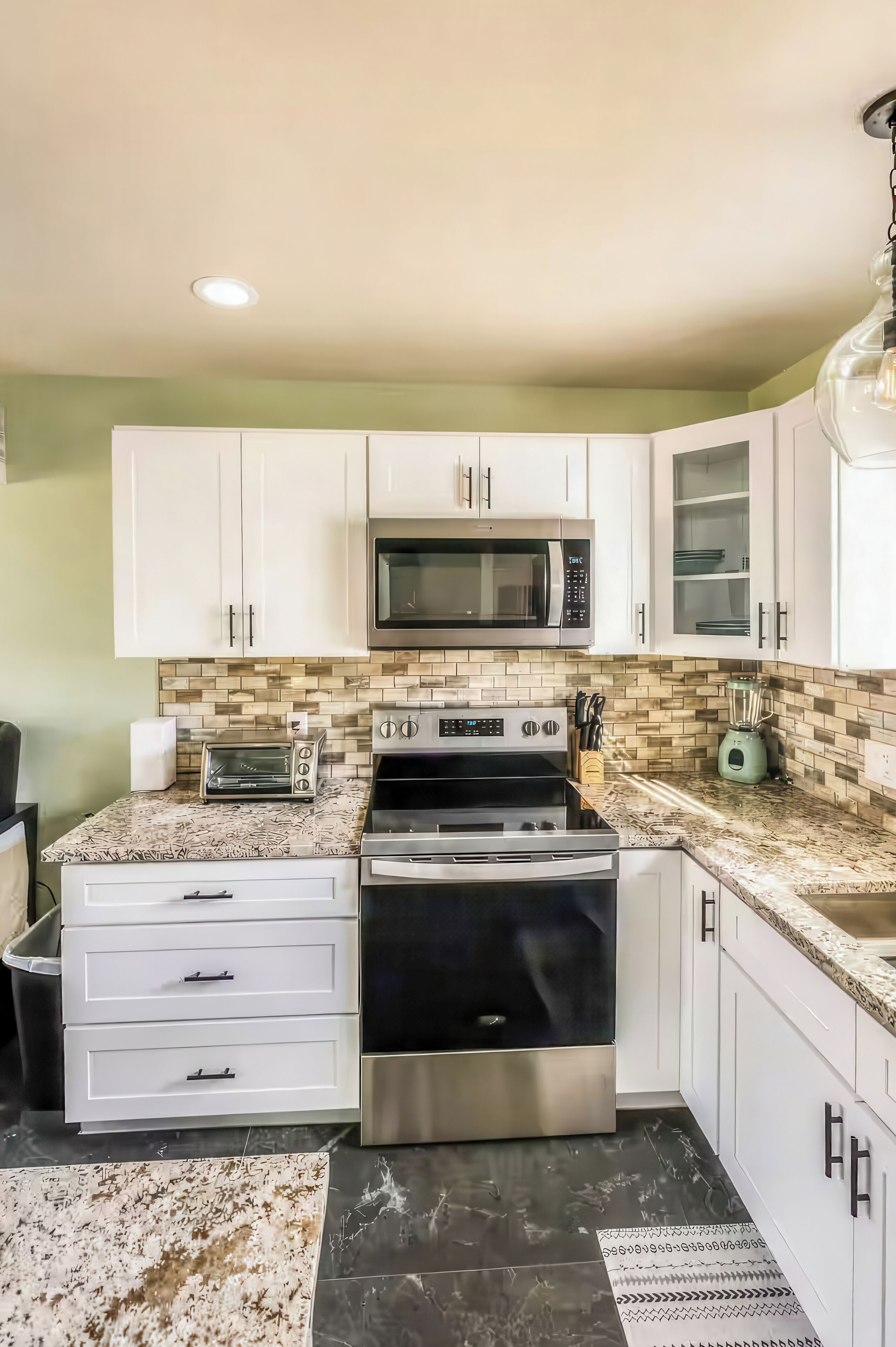 A kitchen with white cabinets, a microwave, a toaster, a stove, and a blender.