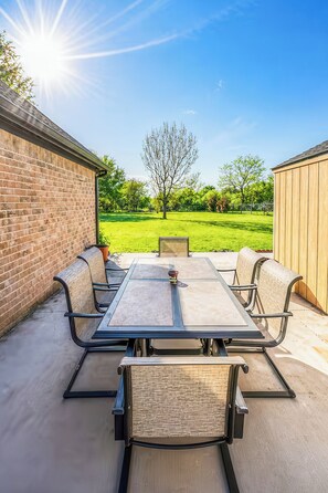 Un patio al aire libre con una mesa, sillas, un muro de ladrillo y un cobertizo de madera.