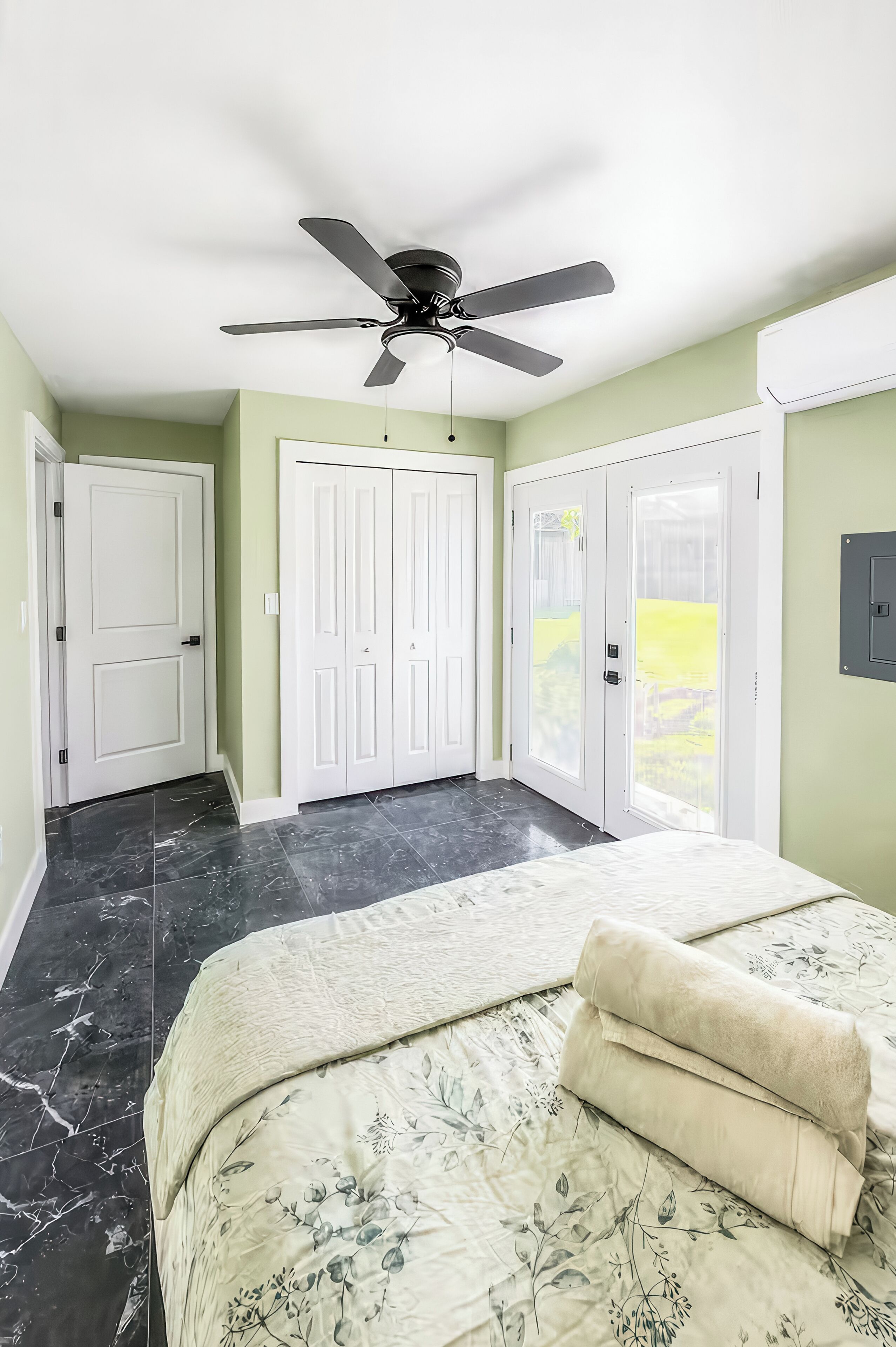 A bedroom with a bed, a ceiling fan, and a view of a green lawn.