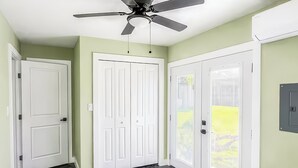A bedroom with a bed, a ceiling fan, and a view of a green lawn.