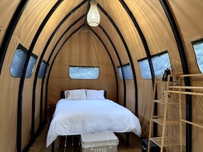 A tent with a bed, a chandelier, and a ladder.