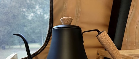 Una tetera negra sobre un soporte de madera con un asa de corcho, ubicada dentro de una estructura parecida a una tienda de campaña.