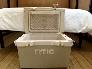 Une glacière blanche et portable, portant la marque « RTIC » sur le côté, est posée sur un plancher en bois.