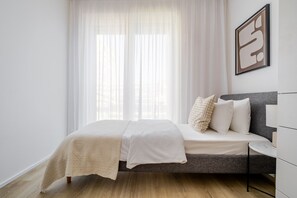 A bedroom with a bed, a bedside table, a window with sheer curtains, and a framed picture on the wall. - Blueground | Prague 7, furnished, close to offices (PRG-12) (Prague)