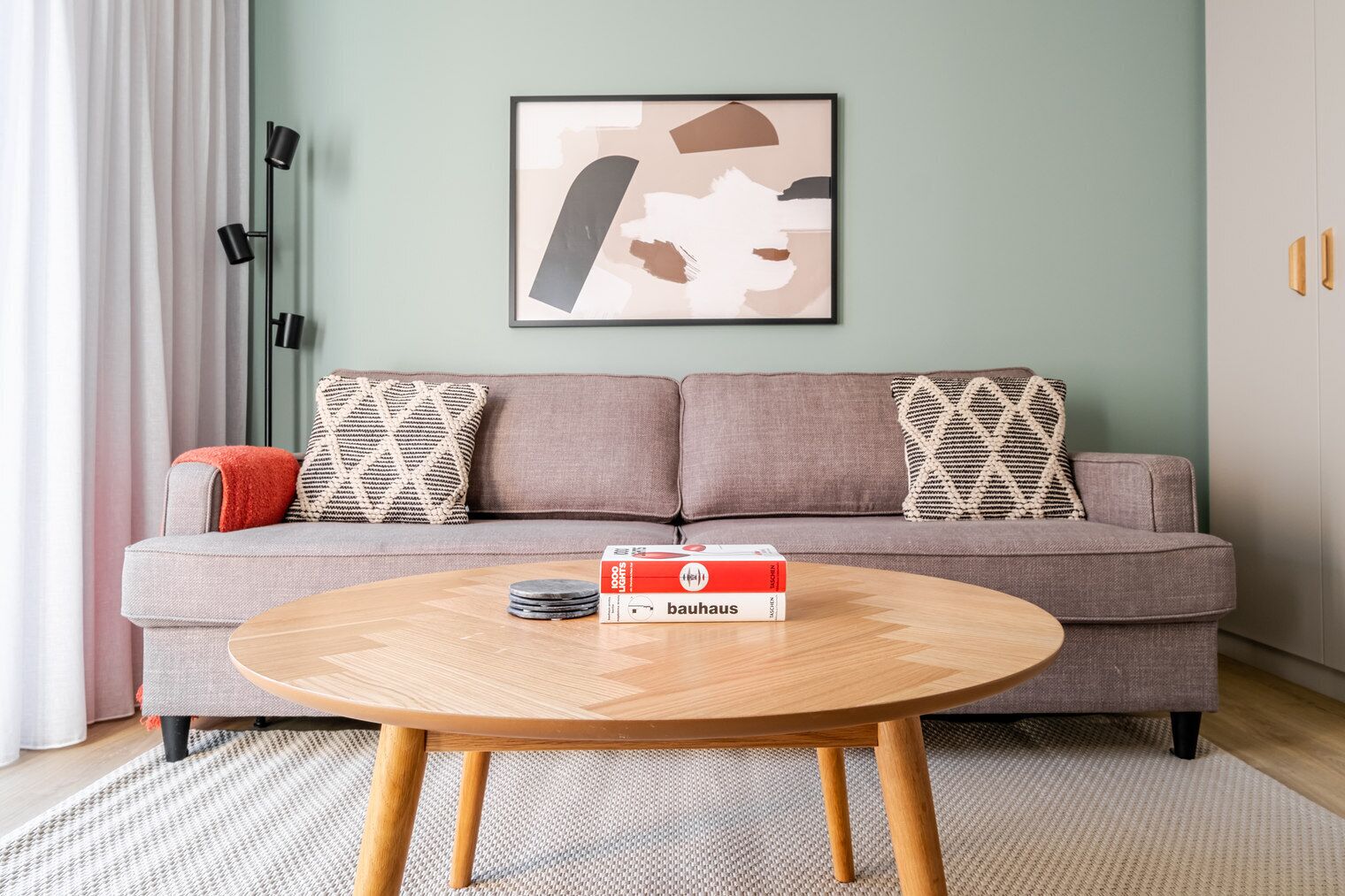 A modern living room with a sofa, patterned cushions, a round wooden coffee table, and a framed abstract artwork on the wall.