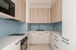 Eine kleine Küche mit Mikrowelle, Backofen, Spüle und hellen Holzschränken.