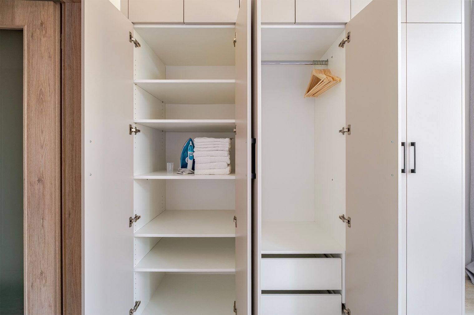 A wardrobe with multiple shelves and hanging space, a wooden door frame, and a metal handle.