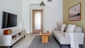 Ett modernt vardagsrum med en platt-TV, ett soffbord i trä, en soffa och en lampa.