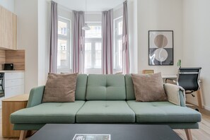 Ein modernes Wohnzimmer mit einem grünen Sofa, einem Essbereich mit Holzschränken und Blick durch große Fenster.