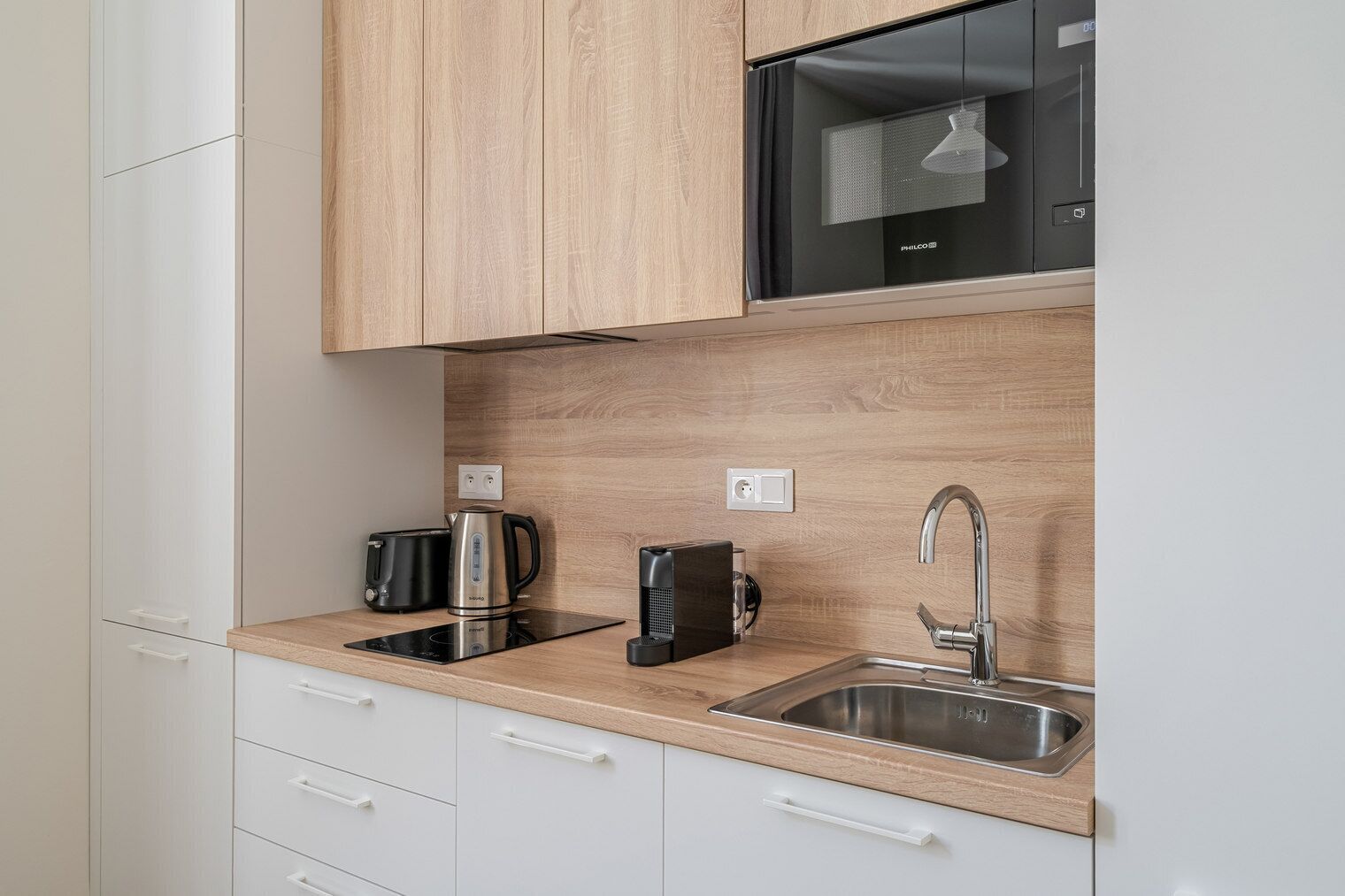 A modern kitchen with a microwave, kettle, coffee maker, and a stainless steel sink.